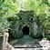 A monster face carved out of stone with an open mouth leading to a dark entrance surrounded by trees